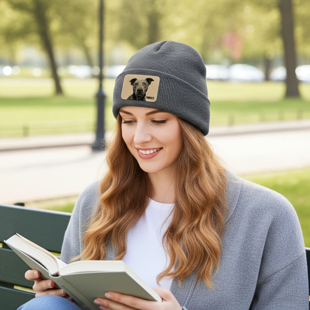 Woman reading a book outdoors wearing a gray beanie with a dog patch.