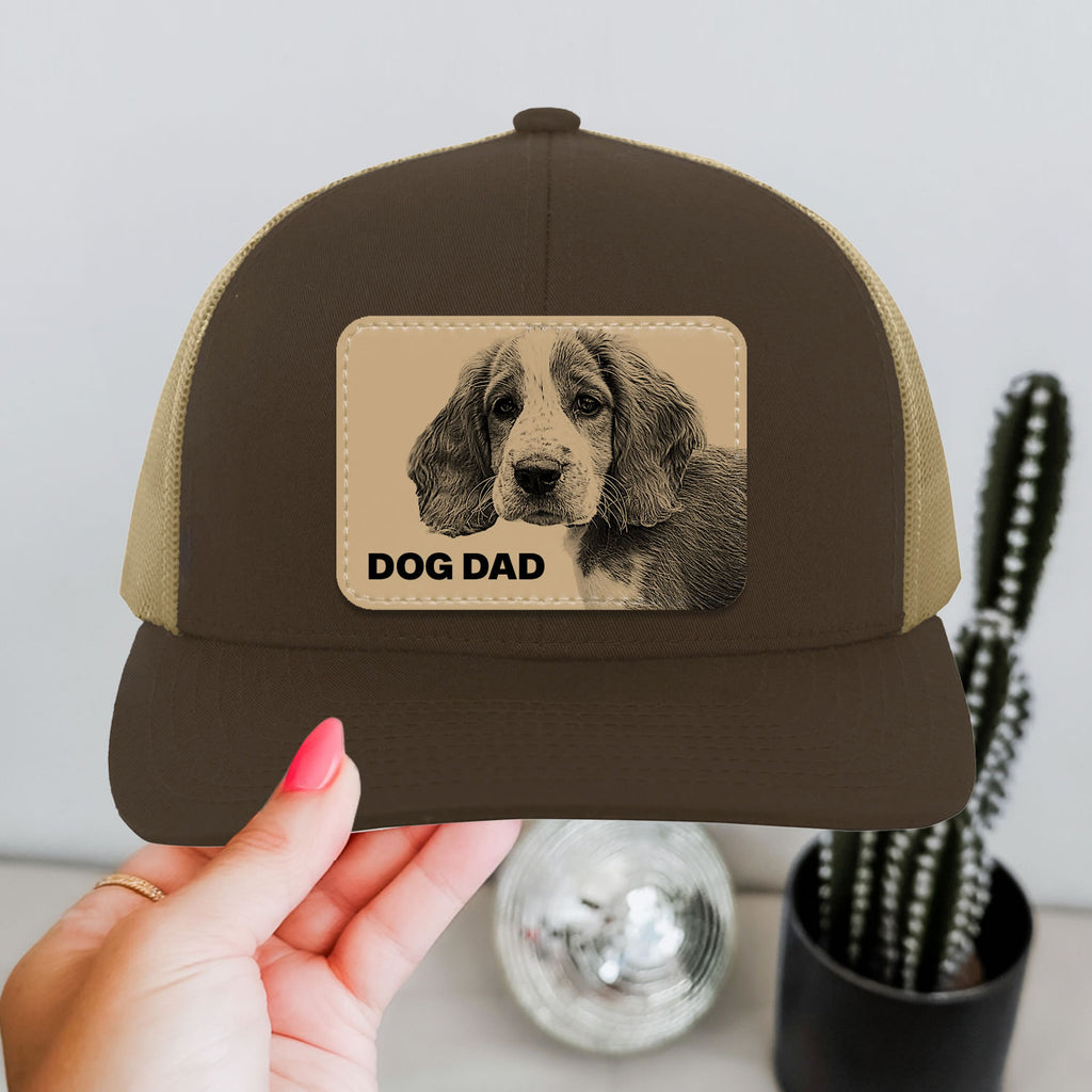 Brown and beige cap with dog dad patch held by a hand