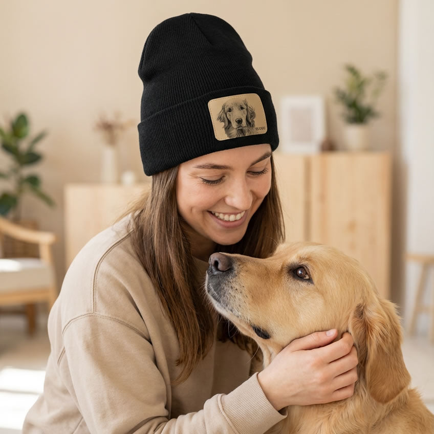 Woman wearing a black beanie with a dog patch, petting a golden retriever indoors.