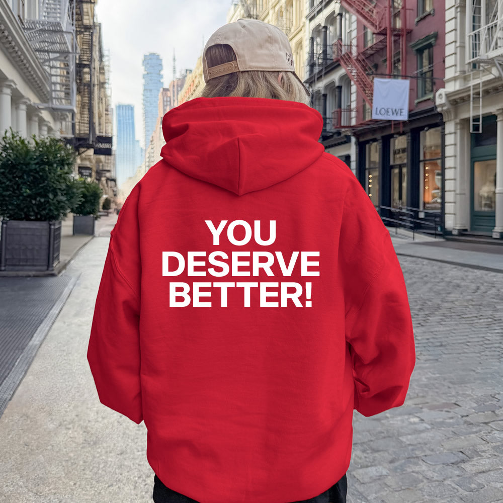 Person wearing a red hoodie with 'YOU DESERVE BETTER!' text on a city street.