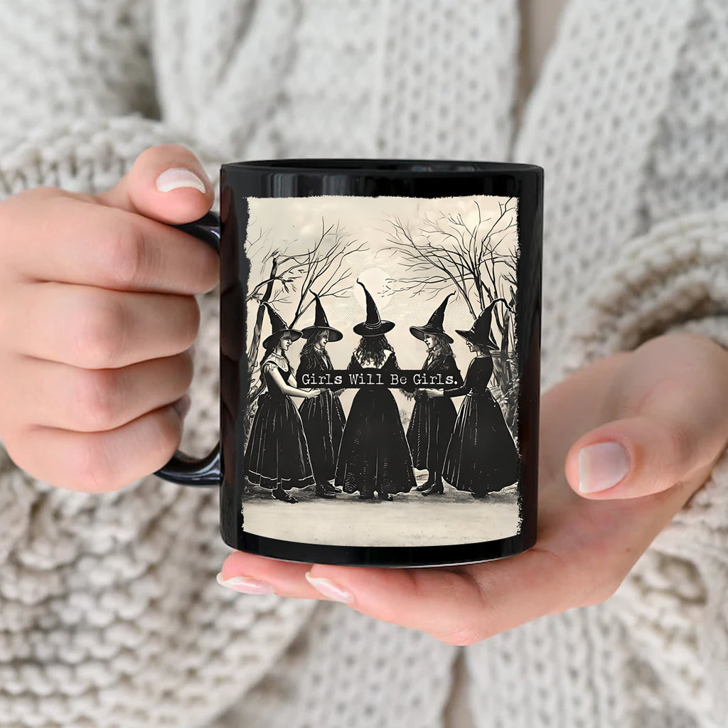 Person holding a mug with a vintage-style design of three women in hats and dresses, with text 'Girls Will Be Girls'.