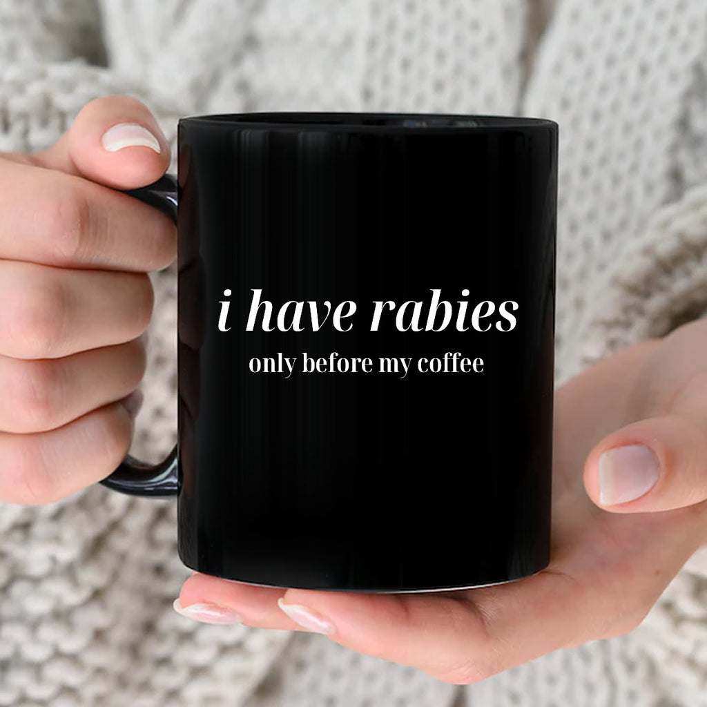 Black mug with 'i have rabies only before my coffee' text held by a person.